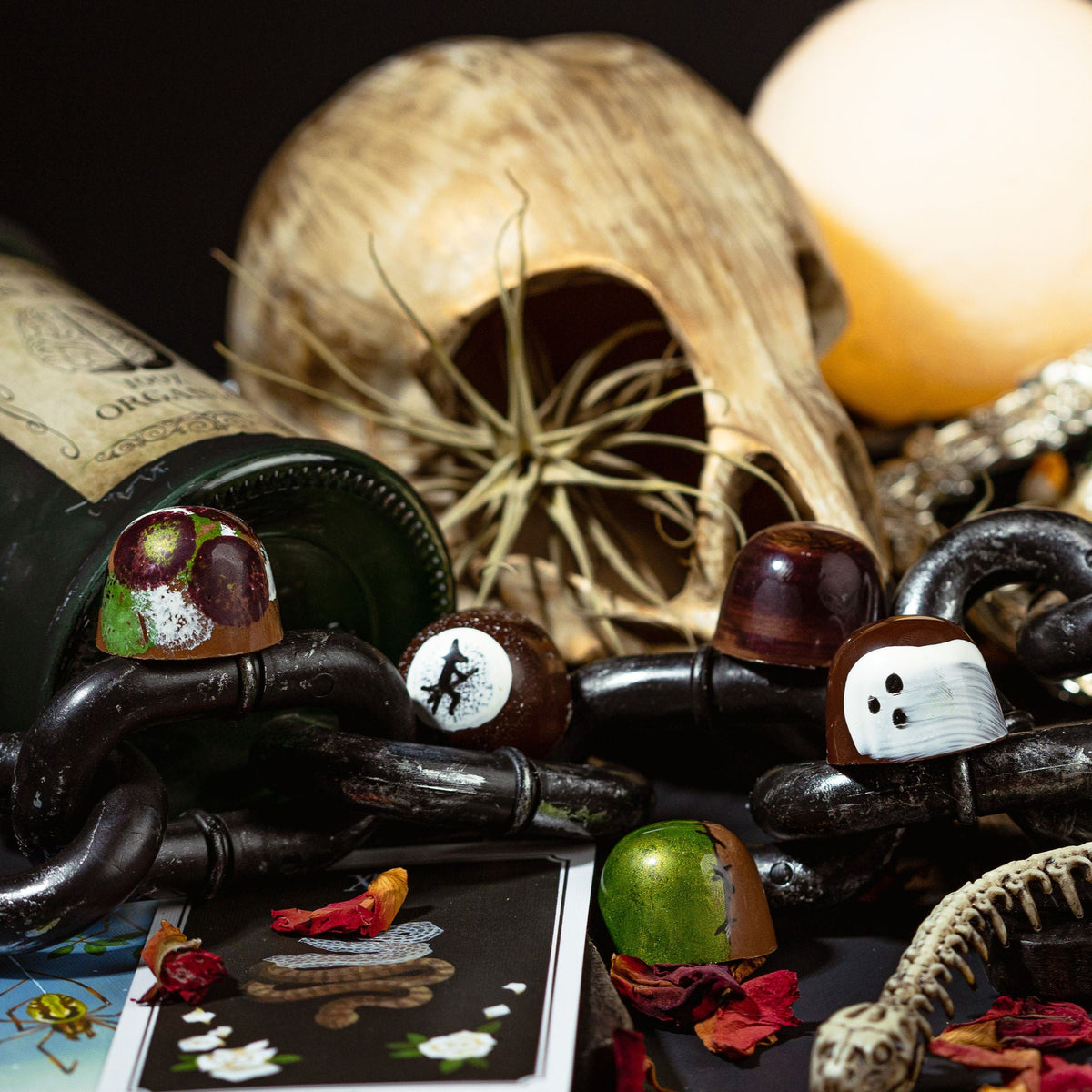 Spooky Halloween decorations including a bottle, chains, and ghost figurines on a dark surface.