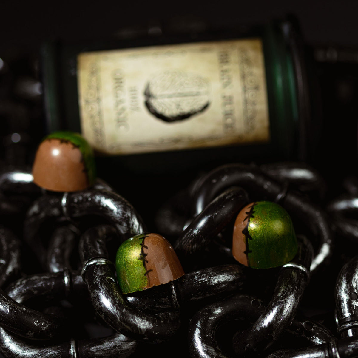Dark chocolate candies with green and brown toppings on a dark background